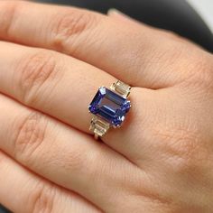 ITEM DESCRIPTION: >> The Ring is made from Solid 14K Yellow Gold. Gemstone used is absolutely natural and ethically sourced. >> Natural Tanzanite in Emerald Cut and octagon & Baguette shape is studded on it with utmost precision. >> This is a minimalist design which makes it a hassle free and everyday jewelry. Gem: Tanzanite Gem size: 10x8mm Gem Weight: 3.424 carats and octagon shape Gem: White Topaz Gem size: 5×2.5, 4×2 mm and Baguette Gem Weight: 0.826 carats Gold purity: 14K (58.33% approx.) Rings With Tanzanite, Luxury Gold Tanzanite Birthstone Ring, Tanzanite Emerald Cut Ring, Emerald Cut Tanzanite Ring, Tanzanite Three Stone Rings As A Gift, Tanzanite Ring Engagement, Tanzanite Rings, Square Engagement Rings, Tanzanite Engagement Ring