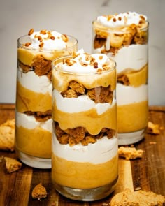 three glasses filled with dessert sitting on top of a wooden table