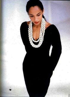 a woman in a black dress with a white beaded necklace and pearls on her neck