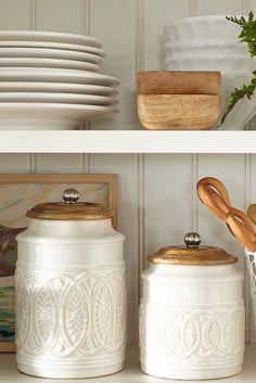 some white jars are sitting on the shelves with wooden spoons and plates in them