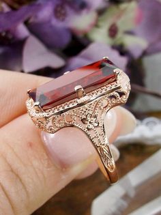 Garnet Cubic Zirconia (CZ) Rose Gold over Sterling Silver Ring 1915 Design#D232 This is a lovely antique Edwardian era inspired filigree ring. This gorgeous ring is set with a stunning garnet cubic zirconia (CZ) gem and overlaid with rose gold plating. The vibrant gemstone is 18mm x 9mm. The ring sits 21mm north-south and 12mm east-west on the finger. The inside of the band is marked 925 for sterling silver. The band and setting have intricate filigree, with hints of floral influence across it. Victorian Rose Gold Ruby Ring, Victorian Ruby Ring For Wedding, Vintage Gold Ruby Ring With Filigree, Victorian Ruby Gemstone Ring For Wedding, Art Deco 14k Gold Filigree Ring As Gift, Vintage Oval Rose Gold Filigree Ring, Victorian Filigree Promise Ring With Intricate Design, Victorian Rose Gold Filigree Ring With Intricate Design, Vintage Rose Gold Ruby Promise Ring