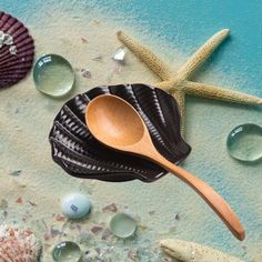 a wooden spoon sitting on top of a sandy beach next to shells and starfish