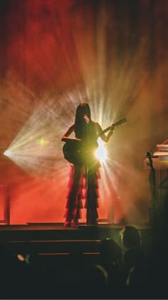 a woman standing on top of a stage with a guitar in her hand and lights behind her