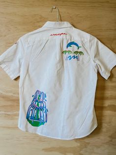 Featuring illustrations by Brooklyn based artist Niege Borges, this is a one of a kind upcycled garment. SIZE + MEASUREMENTS: Length 23", Sleeve 9". High school shirt size M, cotton Care: Wash and dry inside out to preserve your garment. Dry using low heat or hang dry This item was washed and illustrations were transferred onto the garment. Care: Wash and dry inside out to preserve your garment. Dry using low heat or hang dry. Final sale, item cannot be returned. Short Sleeve Reworked Cotton Tops, Upcycled Cotton Short Sleeve Top, Casual Reworked Cotton Shirt, Fitted Shirt, White Button Up, School Fits, School Shirts, Workout Shirts, Final Sale