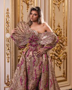 a woman in a gold and pink dress standing next to a golden wall with ornate designs