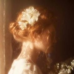 a woman with flowers in her hair looking out the window at the sun shining on her