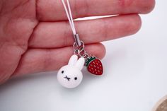 a hand holding a tiny white rabbit with a strawberry on it's ear and wearing a strawberries necklace