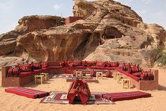 an outdoor seating area in the desert with red couches and rugs on it