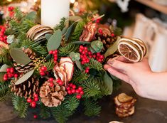 a person is holding a piece of food in front of a christmas centerpiece with pine cones and berries