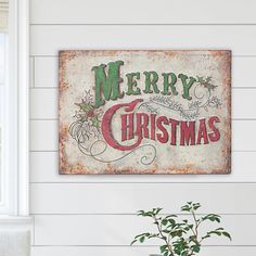 a merry christmas sign hanging on the side of a white wall next to a potted plant