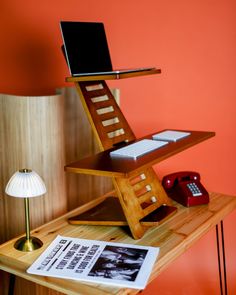 a laptop computer sitting on top of a wooden desk next to a phone and lamp