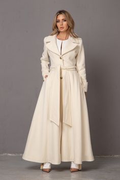 "Crafted in soft winter wool cashmere, this beautiful belted swing overcoat for women is an elegant cover-up this season. Cinched at the waist, this long winter coat will give any lady a stunning princess silhouette that is bound to turn heads! With this maxi satin-lined coat, cozy has never been so chic. KEY FEATURES: - Shoulder pads - Button in the back and on the sleeves - Gorgeous buttoned cuffs - Princess-cut - Floor length - materials: cashmere wool 🌀 IMPORTANT: --Please keep in mind that Long Fall Wedding Outerwear, Fitted Long Cream Wool Coat, Cream Fitted Long Wool Coat, Elegant Winter White Outerwear For Wedding, Elegant Fitted Wool Coat With Belted Cuffs, Elegant Winter White Wool Coat For Fall, Fall Wedding Long Coat, Elegant Belted Wool Coat For Spring, Elegant Formal Wool Coat With Belted Cuffs