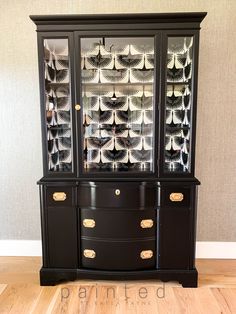 a black china cabinet with glass doors and gold trimmings on the bottom shelf