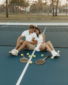 a man and woman sitting on a tennis court with rackets and balls around them