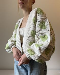 a woman standing in front of a white wall wearing a green and white knitted jacket