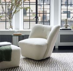 a white chair and ottoman in front of large windows with potted plants on the side