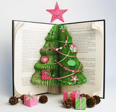 an open book with christmas tree and presents on it, surrounded by pine cones and twinklings