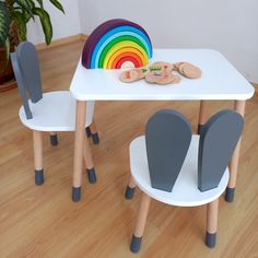 two children's chairs and a table with a rainbow decoration on the top, in front of a potted plant