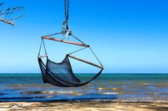 a hammock hanging from a tree over the ocean with blue skies in the background