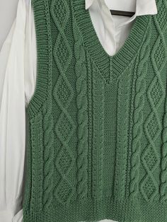 a green sweater vest hanging on a hanger with a white shirt in the background