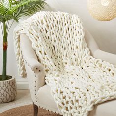 a white chair with a knitted blanket on it next to a potted plant