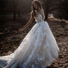 a woman in a wedding dress is walking through the sand with her hand on her hip