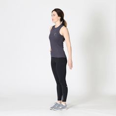 a woman standing in front of a white background wearing black leggings and a gray tank top