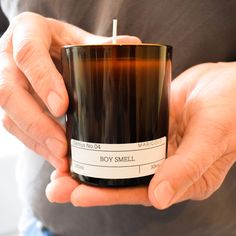 a man holding a candle in his hands with the label on it that says boy smell