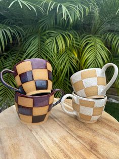 two coffee cups sitting on top of a wooden table next to each other with palm trees in the background