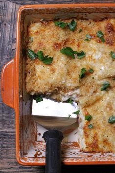 an orange casserole dish with cheese and herbs on top, next to a spatula