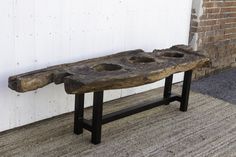 a wooden bench with two holes in the middle on carpeted floor next to brick wall