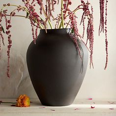 a black vase with pink flowers in it on a table next to a white wall