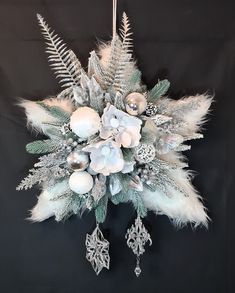 a christmas ornament with white flowers and silver ornaments hanging on a black background