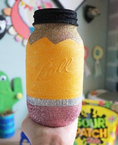 a hand holding up a jar filled with colored sand and glitter on top of it