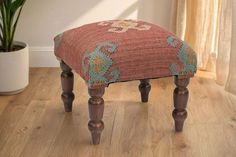 a small wooden stool sitting on top of a hard wood floor next to a potted plant