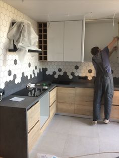 a man in overalls is painting the kitchen wall with white tiles and wooden cabinets