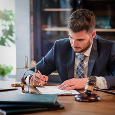 a man in a suit sitting at a desk writing on paper with a judge's gavel next to him