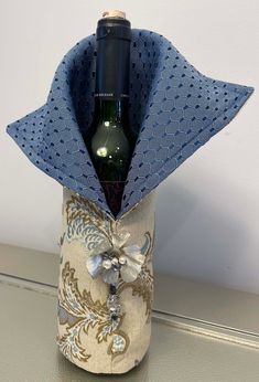 a wine bottle wrapped in blue fabric with a bow on the top, and an empty beer bottle inside it