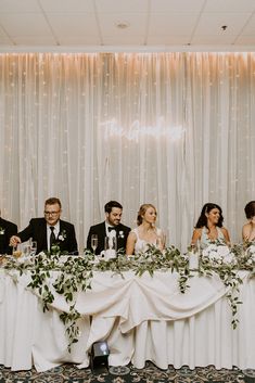 a group of people sitting at a table with flowers and greenery on the table