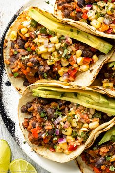 four tacos on a plate with limes and cilantro in the background