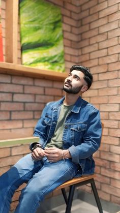 a man sitting on top of a wooden chair in front of a brick wall and window