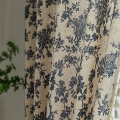 a close up of a curtain with blue flowers on it and a potted plant in the background