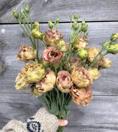 a hand holding a bouquet of flowers on top of a wooden table next to a glove