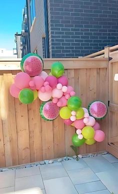 some balloons and watermelon are hanging on a fence