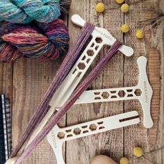 three skeins of yarn sitting on top of a wooden table next to knitting needles