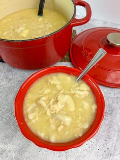 two red bowls filled with soup on top of a counter next to a pot and ladle