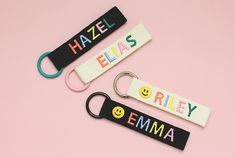 three personalized keychains on a pink background with the words hazel, ellas, smiley and emma