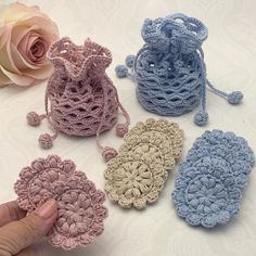 four crocheted purses sitting on top of a table next to a pink rose