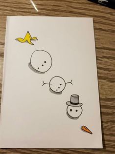 a drawing of two snowmen and a banana sitting on top of a wooden table