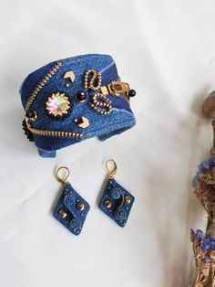 a blue hat, earrings and bracelet on a white surface next to some dried flowers